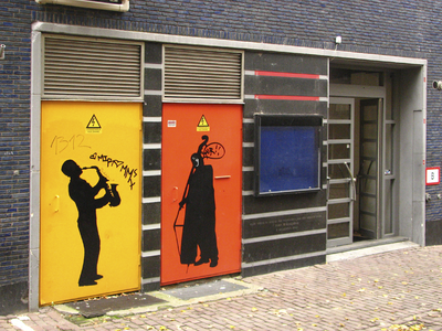 872062 Gezicht op de ingang van het voormalige jazzpodium SJU-Huis (Varkenmarkt 2) te Utrecht, met op de deuren links ...